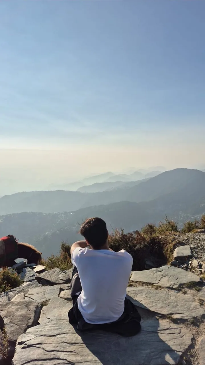Anshum Singla sitting on a mountain ridge, looking out over the hills